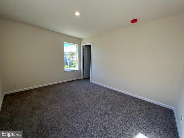 empty room featuring dark colored carpet, visible vents, and baseboards