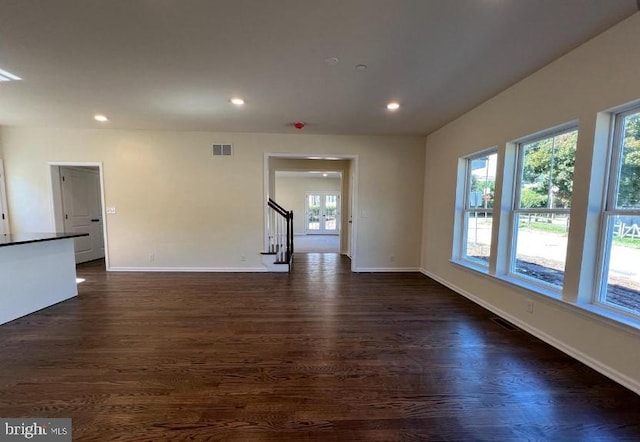 unfurnished room featuring visible vents, dark wood-type flooring, a healthy amount of sunlight, and stairway