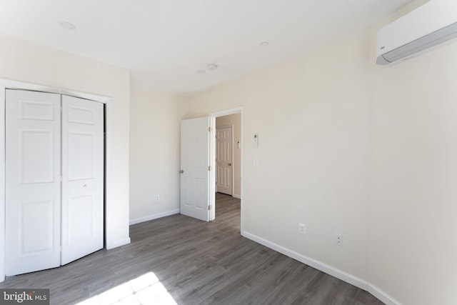 unfurnished bedroom with a closet, a wall unit AC, and hardwood / wood-style flooring