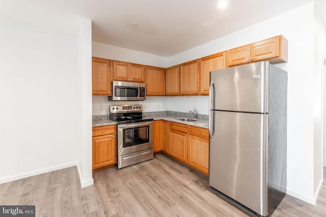 kitchen with light stone countertops, appliances with stainless steel finishes, light hardwood / wood-style flooring, and sink