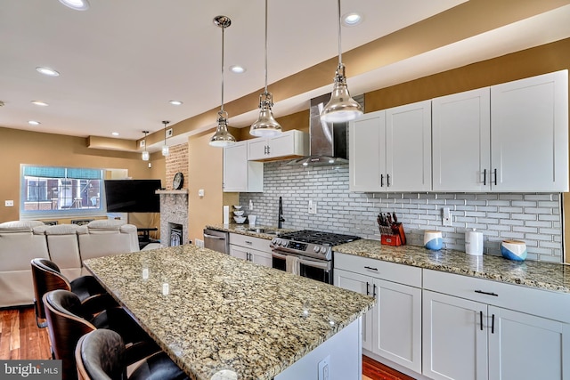 kitchen featuring wall chimney range hood, white cabinetry, a center island, gas range, and decorative light fixtures