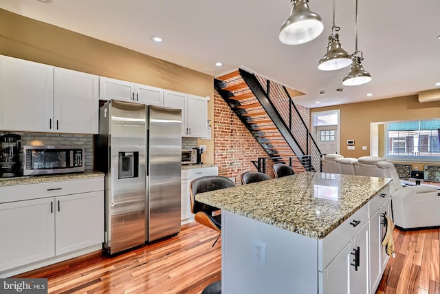 kitchen featuring a kitchen island, appliances with stainless steel finishes, pendant lighting, white cabinetry, and light hardwood / wood-style flooring