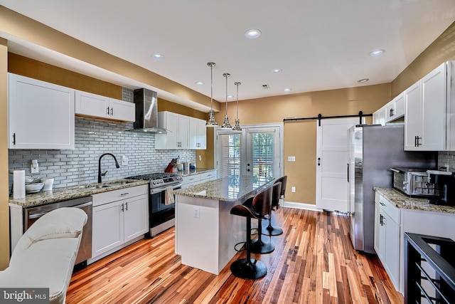 kitchen with wall chimney exhaust hood, white cabinetry, stainless steel appliances, and a barn door