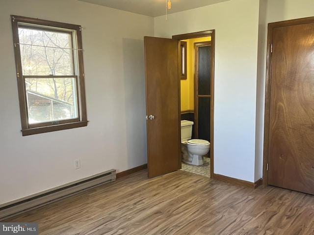 unfurnished bedroom featuring ensuite bath, wood-type flooring, and a baseboard heating unit