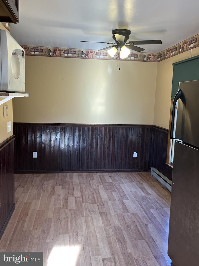 kitchen with light hardwood / wood-style flooring, stainless steel refrigerator, a baseboard heating unit, and wood walls