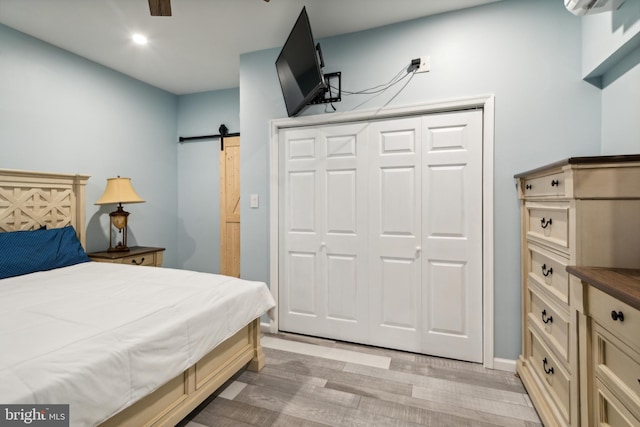 bedroom featuring ceiling fan, a barn door, light wood-type flooring, and a closet