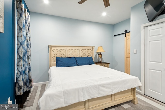 bedroom featuring ceiling fan, light wood-type flooring, and a barn door