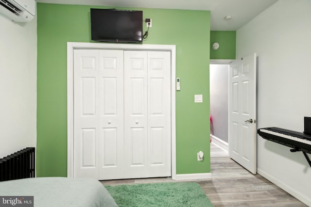 bedroom featuring radiator, light hardwood / wood-style flooring, a closet, and a wall mounted air conditioner