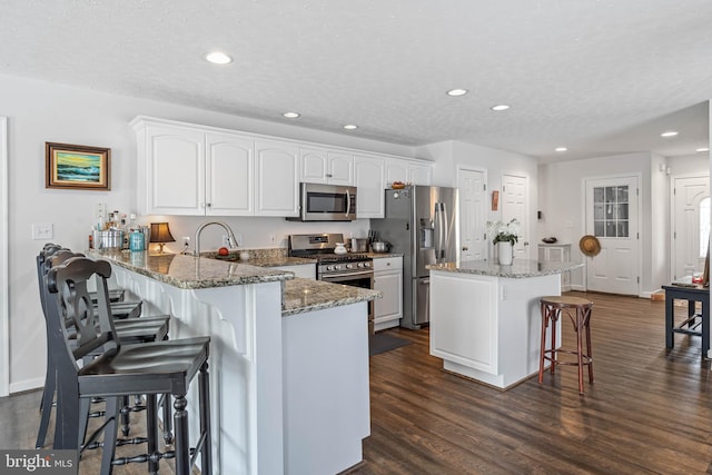 kitchen with dark stone counters, dark hardwood / wood-style floors, white cabinetry, kitchen peninsula, and stainless steel appliances