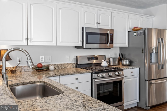 kitchen with dark wood-type flooring, white cabinets, light stone counters, sink, and stainless steel appliances