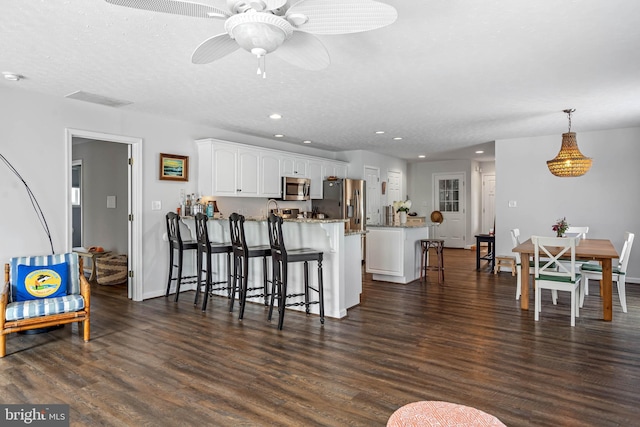 kitchen featuring ceiling fan, a kitchen breakfast bar, dark hardwood / wood-style flooring, white cabinets, and appliances with stainless steel finishes