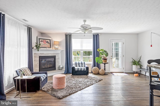 living room with a textured ceiling, ceiling fan, a stone fireplace, and hardwood / wood-style flooring