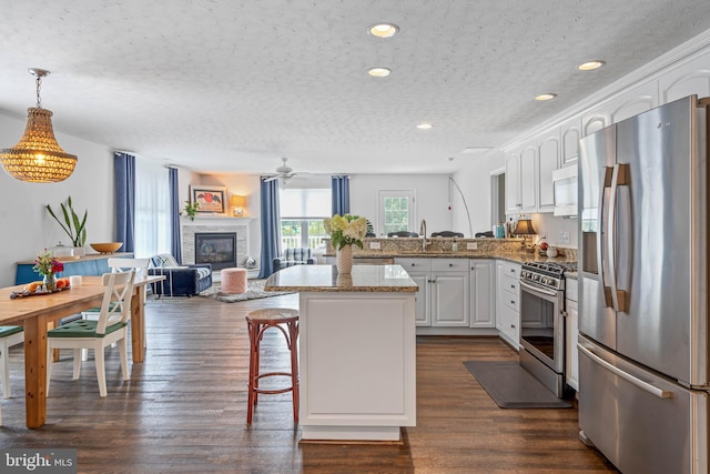 kitchen featuring appliances with stainless steel finishes, light stone countertops, dark hardwood / wood-style floors, white cabinetry, and hanging light fixtures