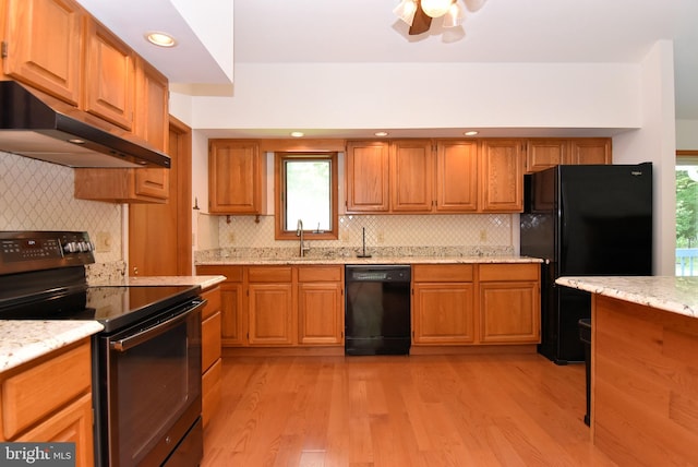 kitchen with light hardwood / wood-style floors, sink, light stone counters, and black appliances