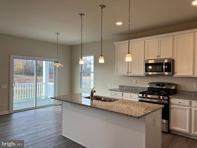 kitchen featuring white cabinets, decorative light fixtures, appliances with stainless steel finishes, sink, and a center island with sink