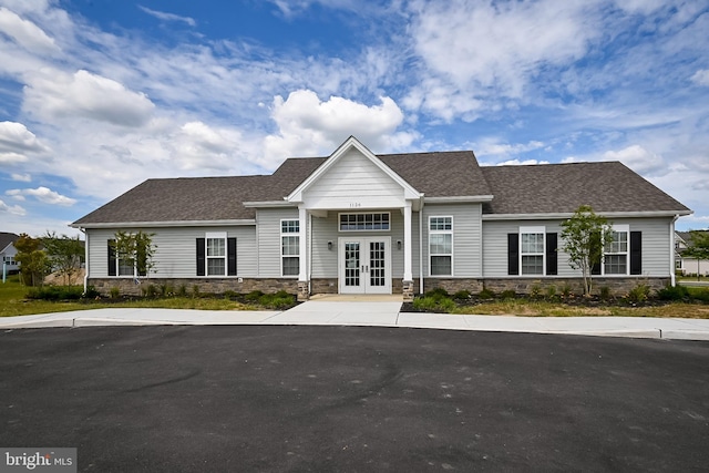 view of front of home featuring stone siding, french doors, and roof with shingles