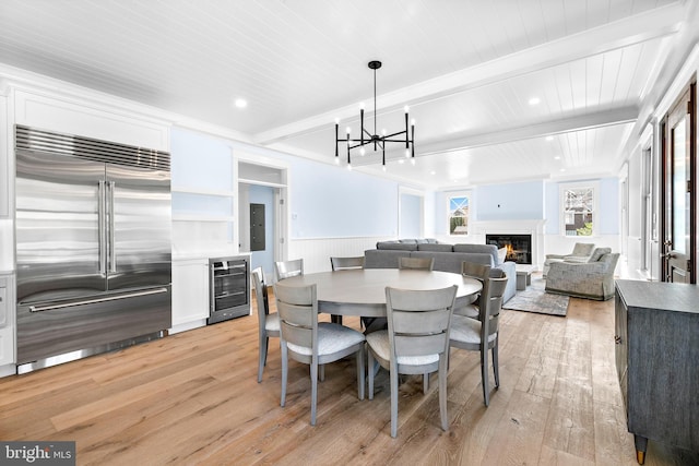 dining room with a glass covered fireplace, beverage cooler, light wood-style flooring, and beam ceiling