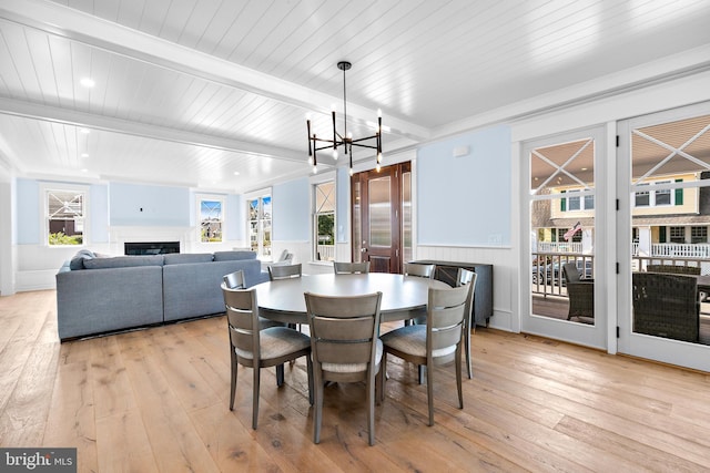 dining area with light wood-type flooring, plenty of natural light, beamed ceiling, and a chandelier