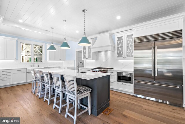 kitchen with custom range hood, white cabinetry, light hardwood / wood-style floors, and stainless steel appliances