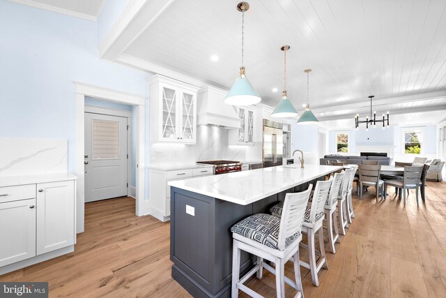 kitchen featuring premium range hood, a center island with sink, white cabinets, and light wood-type flooring