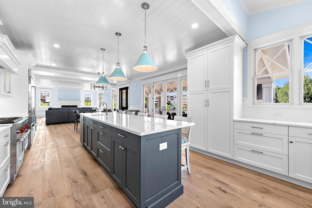 kitchen with hanging light fixtures, open floor plan, a kitchen island with sink, white cabinetry, and high end stove