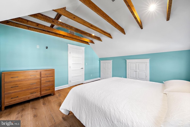 bedroom with light wood-style floors, lofted ceiling with beams, and baseboards