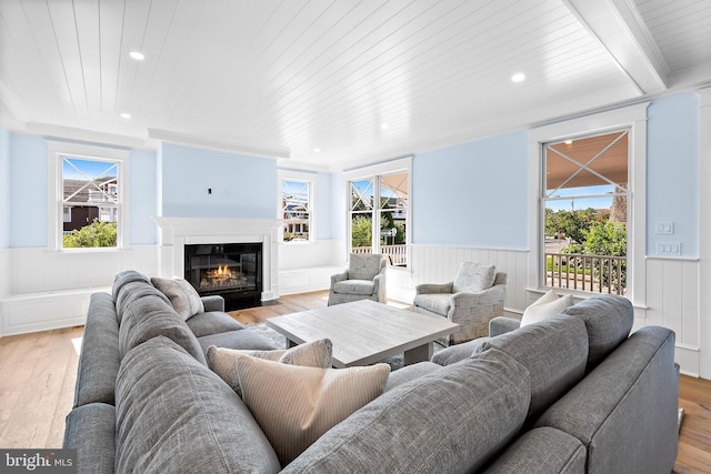 living room featuring a wainscoted wall, wooden ceiling, a fireplace with flush hearth, and light wood-style flooring