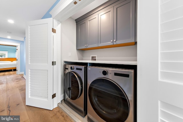 clothes washing area featuring recessed lighting, cabinet space, light wood-style flooring, washing machine and dryer, and baseboards