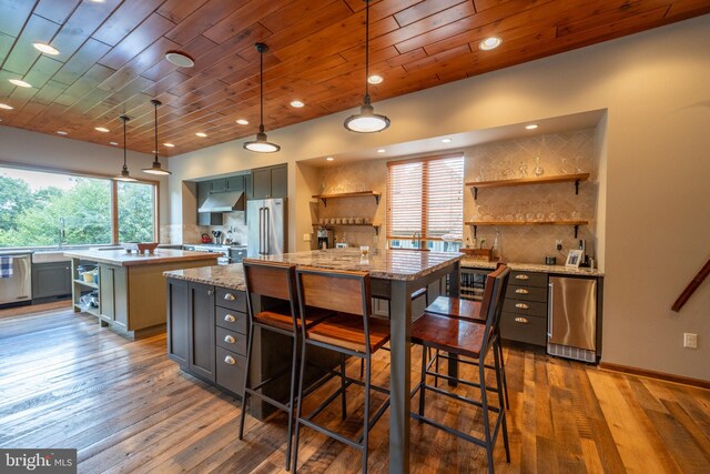 kitchen with appliances with stainless steel finishes, a center island, dark hardwood / wood-style floors, and pendant lighting