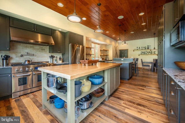 kitchen featuring premium appliances, wood-type flooring, a kitchen island, hanging light fixtures, and butcher block counters