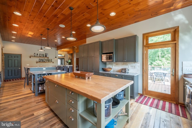 kitchen featuring light wood-type flooring, tasteful backsplash, decorative light fixtures, a kitchen island, and butcher block counters