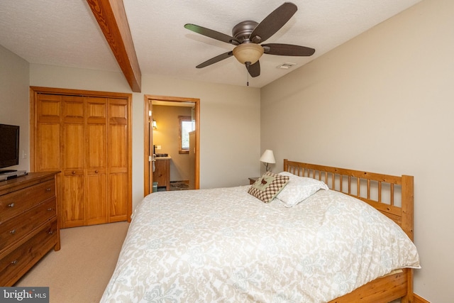 carpeted bedroom with ensuite bathroom, ceiling fan, a textured ceiling, beam ceiling, and a closet