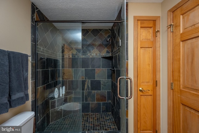 bathroom with toilet, a shower with door, and a textured ceiling