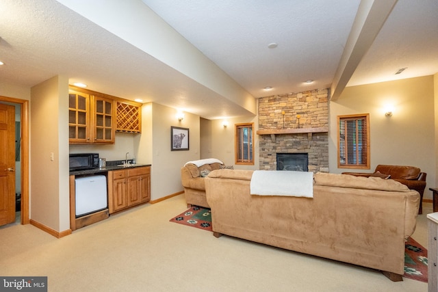 living room featuring a stone fireplace, light colored carpet, a textured ceiling, and indoor wet bar