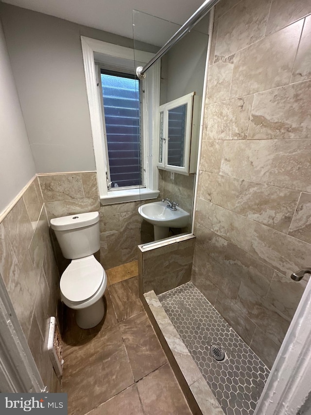 bathroom with tile patterned flooring, sink, a tile shower, toilet, and tile walls