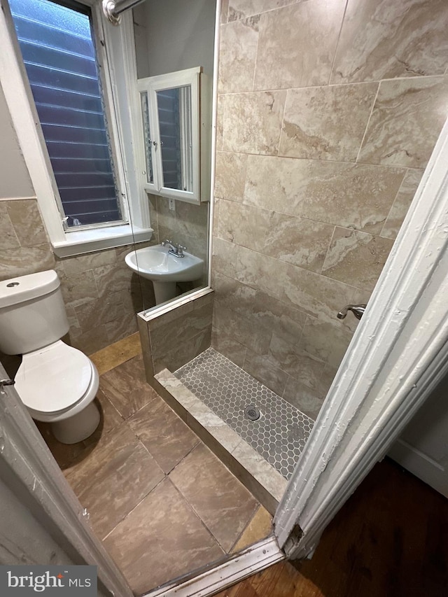 bathroom with sink, toilet, tiled shower, and tile walls