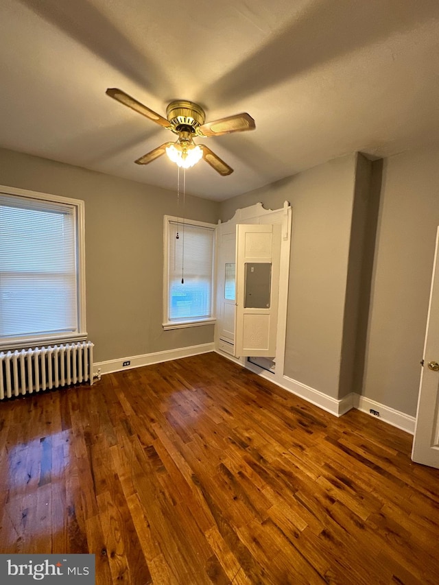 unfurnished room featuring dark wood-type flooring, ceiling fan, and radiator heating unit