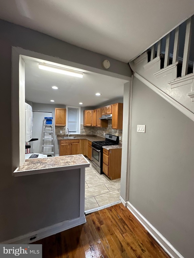 kitchen featuring tasteful backsplash, stainless steel stove, sink, kitchen peninsula, and light hardwood / wood-style flooring