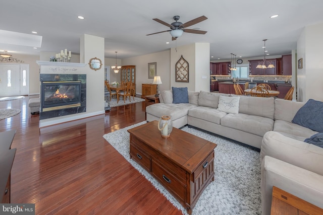 living room with baseboards, a tiled fireplace, recessed lighting, ceiling fan with notable chandelier, and wood finished floors