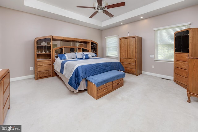 bedroom with baseboards, a raised ceiling, light colored carpet, and multiple windows