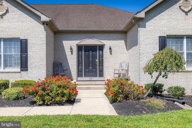 property entrance featuring brick siding and roof with shingles