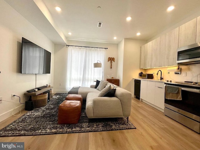 interior space featuring appliances with stainless steel finishes, light brown cabinetry, light hardwood / wood-style floors, and dark stone countertops