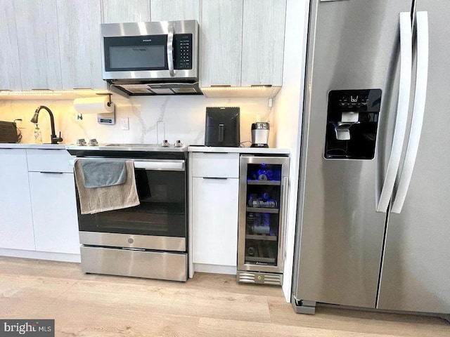 kitchen with beverage cooler, stainless steel appliances, and light hardwood / wood-style flooring