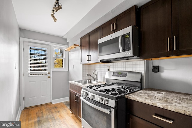 kitchen with sink, tasteful backsplash, dark brown cabinets, stainless steel appliances, and light hardwood / wood-style floors