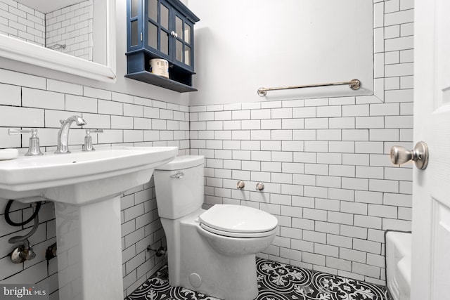 bathroom with a tub, sink, tile walls, and toilet