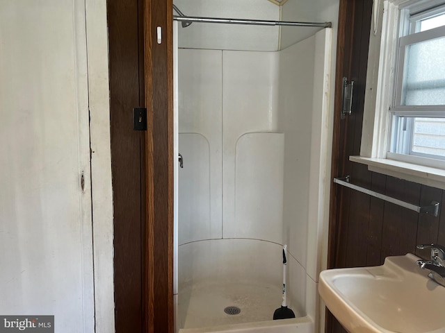 bathroom featuring a healthy amount of sunlight, a shower, sink, and wooden walls