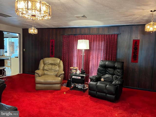 sitting room featuring wood walls, a notable chandelier, a textured ceiling, and carpet floors