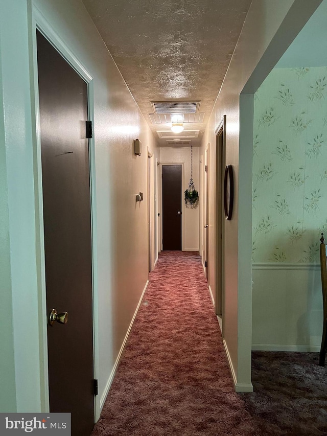 hallway featuring dark carpet and a textured ceiling