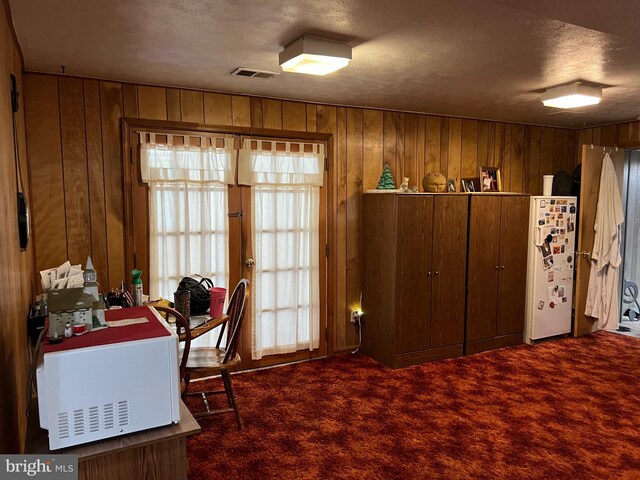 carpeted office space featuring a textured ceiling and wooden walls