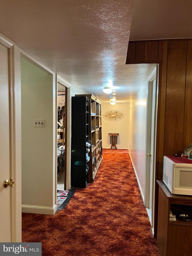 hall with a textured ceiling, wooden walls, and carpet floors